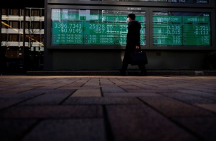 A man wearing a protective mask, amid the coronavirus disease (COVID-19) outbreak, walks past an electronic board displaying Shanghai Composite index, Nikkei index and Dow Jones Industrial Average outside a brokerage in Tokyo, Japan, March 7, 2022. REUTER